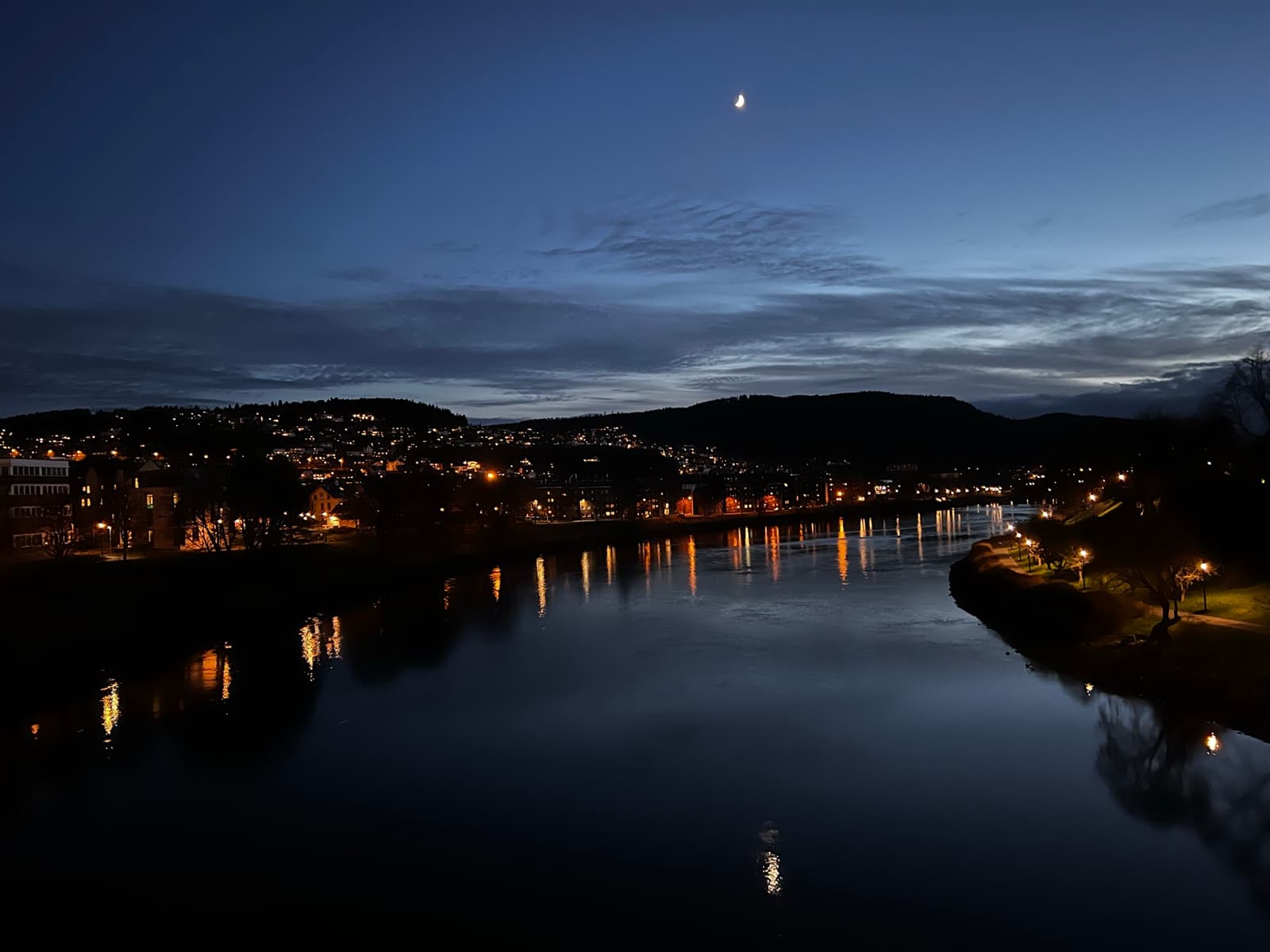 Town lights reflected on a river beneath a crescent moon